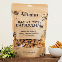 Bag of Kiwi Artisan Manuka Honey Macadamias on a wooden surface with a bowl of macadamias.