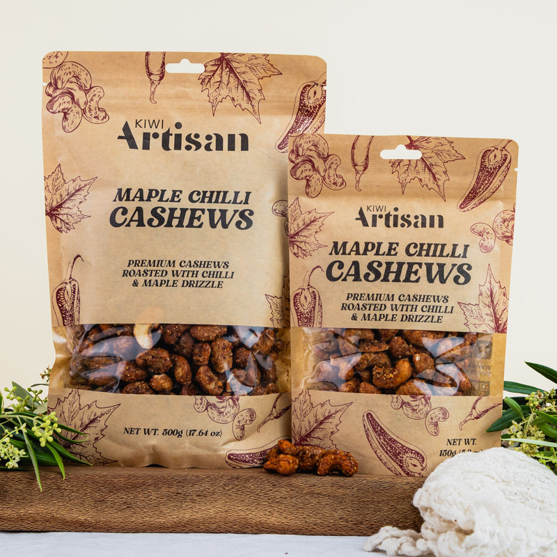 Two packages of Kiwi Artisan Maple Chilli Cashews on a wooden board with a white background.