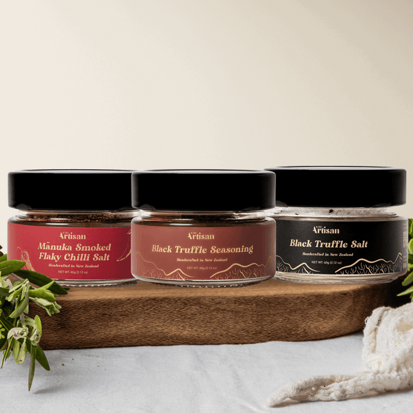 Three jars of Kiwi Artisan Truffle salt and truffle seasoning and manuka smoked flaky  chilli salt on a wooden board with a white background