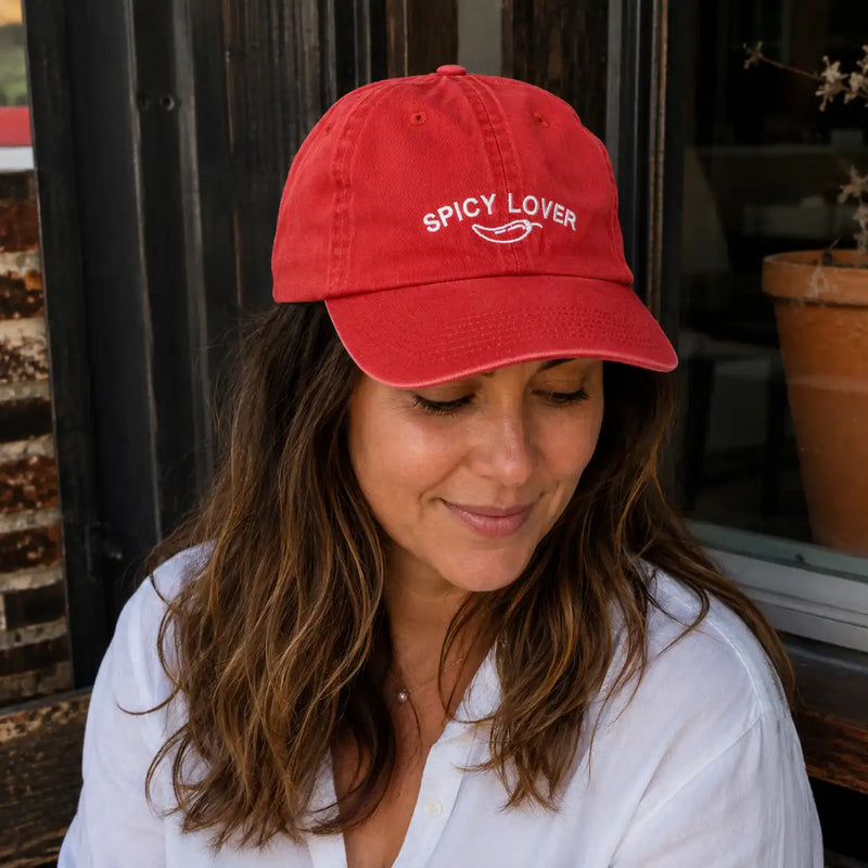 Woman wearing a red cap with 'Spicy Lover' text, sitting outdoors.